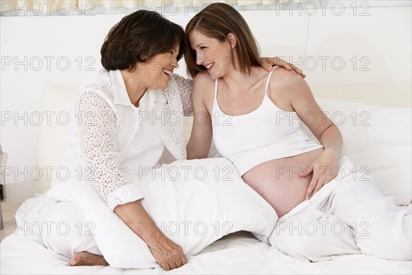 Mother hugging pregnant daughter on bed