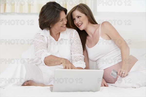 Mother and pregnant daughter using laptop