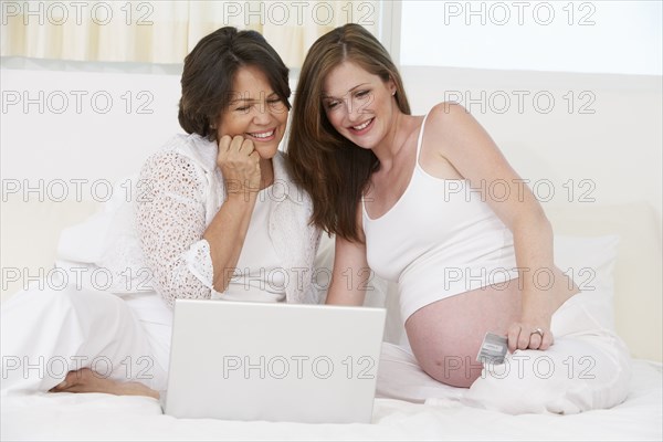 Mother and pregnant daughter using laptop