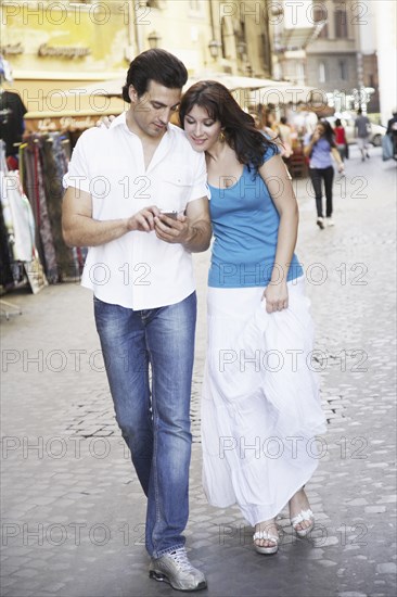 Caucasian couple using cell phone on city street