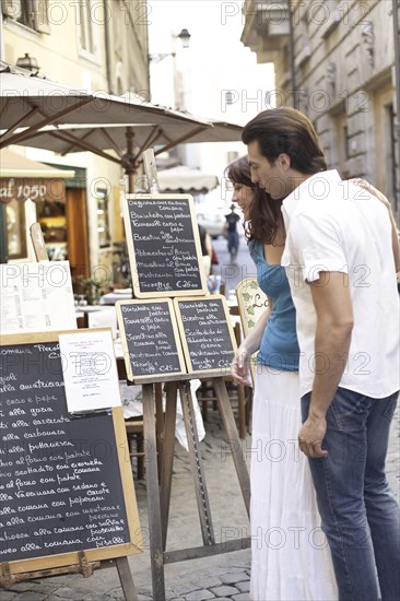 Caucasian couple reading menus on city street