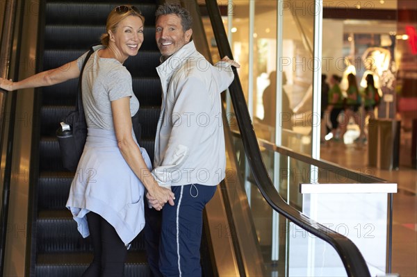 Caucasian couple riding escalator in shopping mall