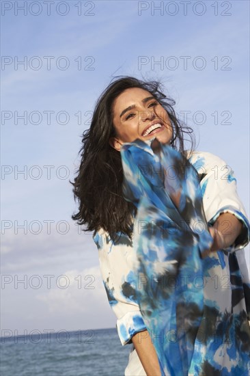 Hispanic woman playing with blue fabric on beach