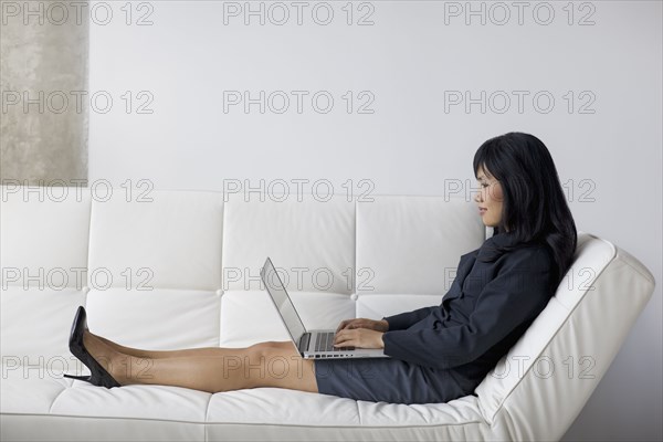 Businesswoman with feet up using laptop on sofa