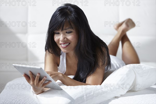 Woman laying on bed using digital tablet