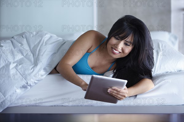 Woman laying in bed using digital tablet