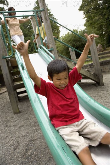 Asian boy sliding down slide on playground