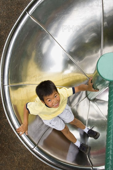 Asian boy sliding down circular slide