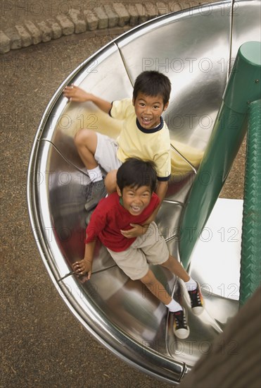 Asian boys sliding down circular slide