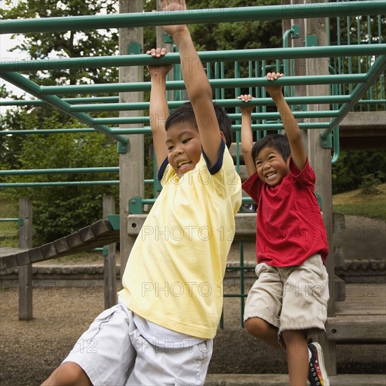 Asian boys crossing monkey bars on playground