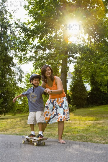 Asian mother helping son learn to skateboard