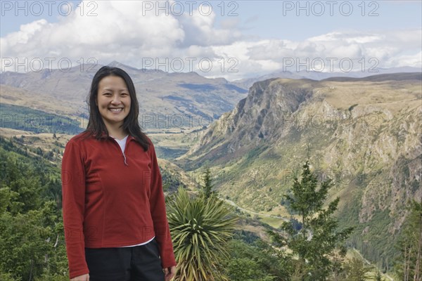 Chinese woman standing on hilltop with remote valley in distance