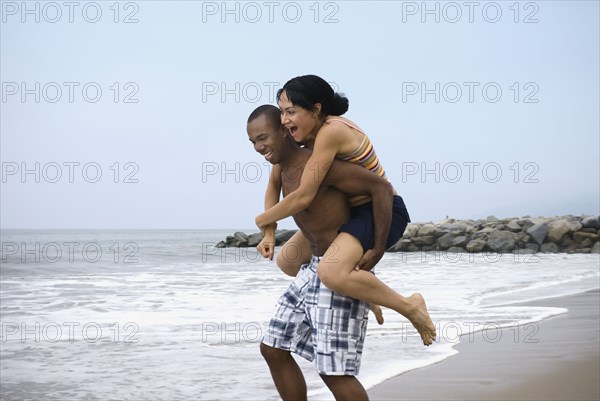 African man giving girlfriend piggy back ride at beach