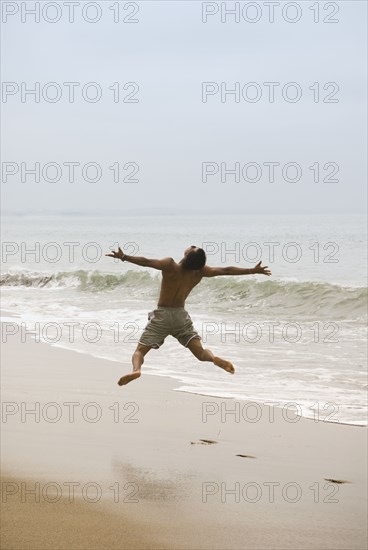 Mixed race man jumping in air on beach