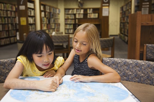 Girls looking at atlas in library