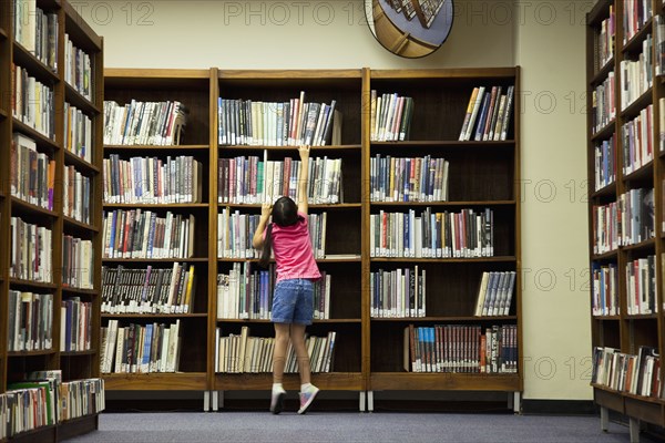 Girl reaching for book on library shelf