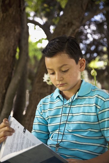 Mixed race boy reading book outdoors