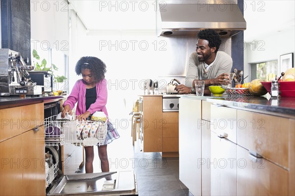 Father watching daughter loading dishwasher