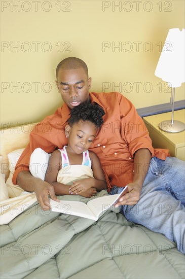 Black father reading book to daughter in bedroom