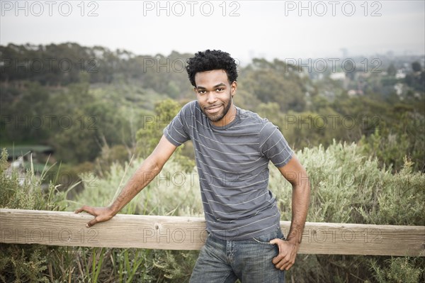 African American man leaning on fence in remote area