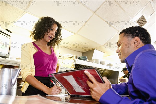 Waitress taking order from man with menu at diner counter