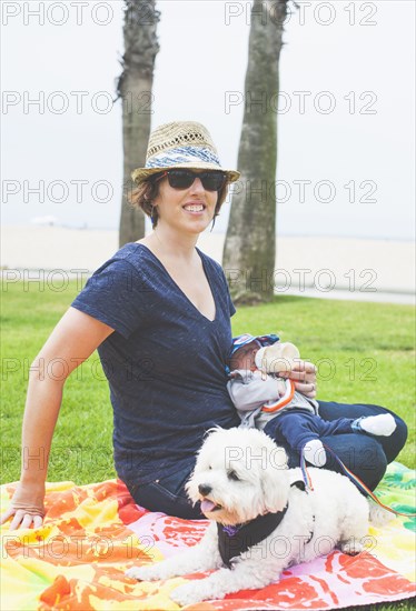 Mother and newborn baby sitting with dog in park