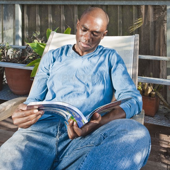 Black man reading book on patio