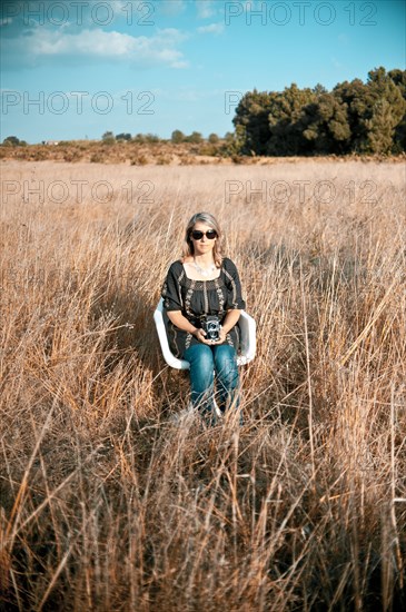 Caucasian woman sitting in field with old-fashioned camera