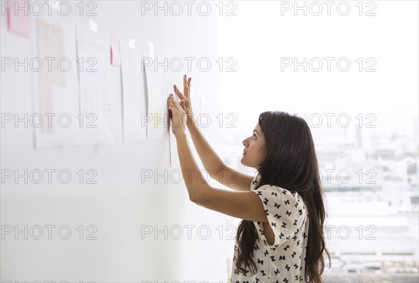 Businesswoman taping up papers on office wall