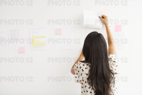 Businesswoman taping up papers on office wall