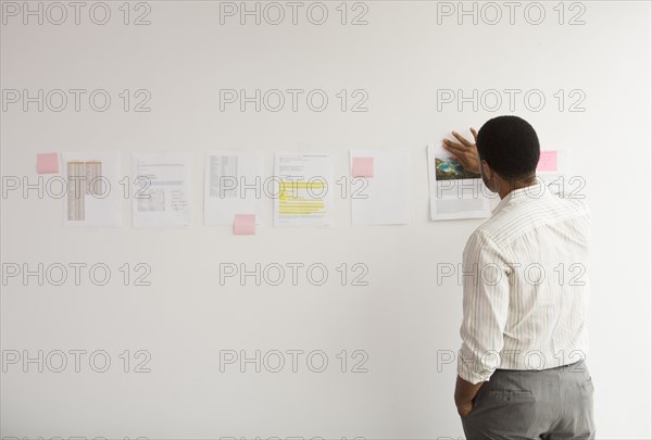 Black businessman taping up papers on office wall