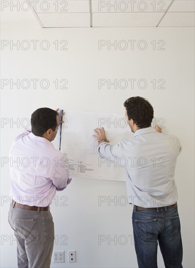Hispanic businessmen examining blueprints in office