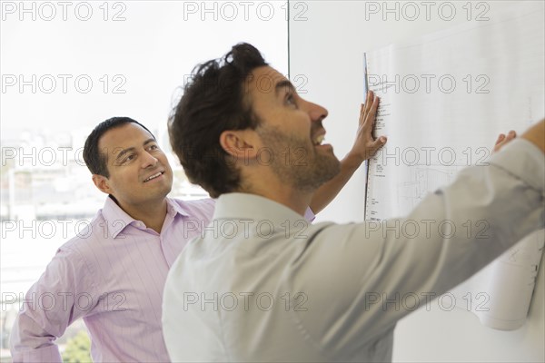 Hispanic businessmen examining blueprints in office