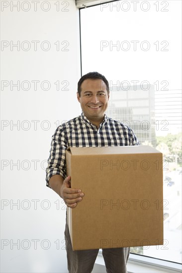 Hispanic businessman carrying cardboard box in office