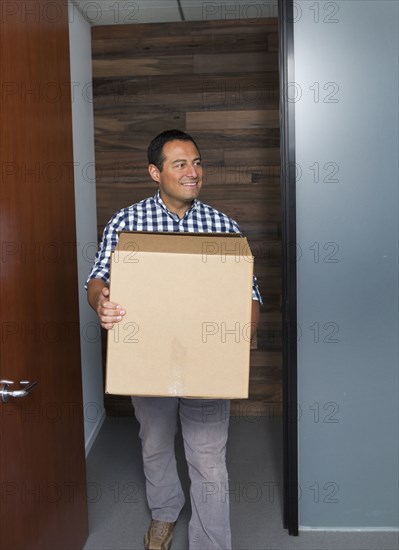 Hispanic businessman carrying cardboard box in office