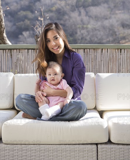 Mother holding baby girl on patio sofa