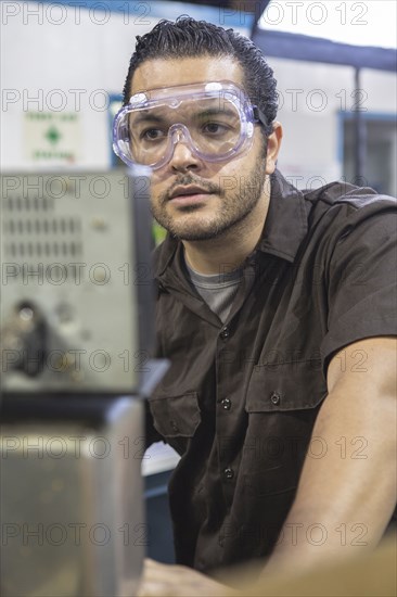 Hispanic worker operating machinery in factory