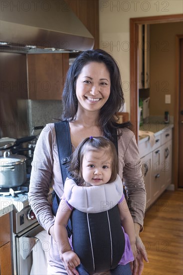 Mother holding daughter in sling in kitchen