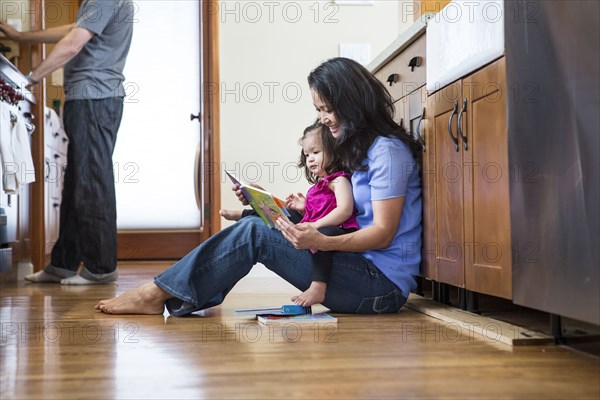 Mother reading to daughter in kitchen