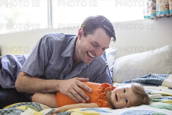 Caucasian father playing with daughter on bed