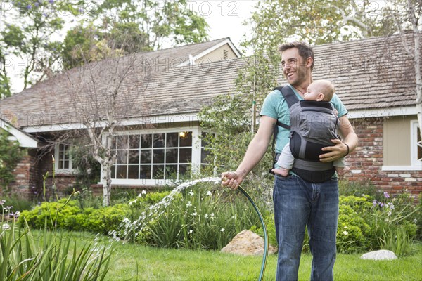 Caucasian father holding baby and watering plants