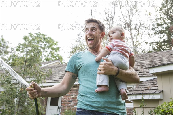 Caucasian father holding baby and watering plants