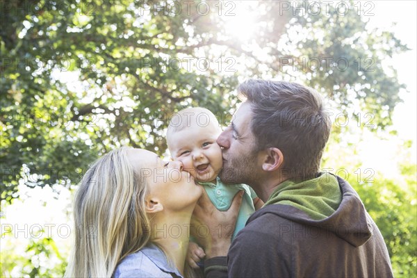 Caucasian couple kissing baby in backyard