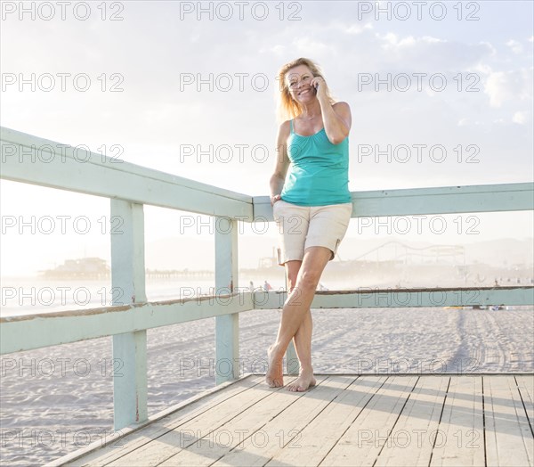 Caucasian woman talking on cell phone on boardwalk at beach