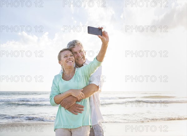 Caucasian couple taking cell phone selfie on beach