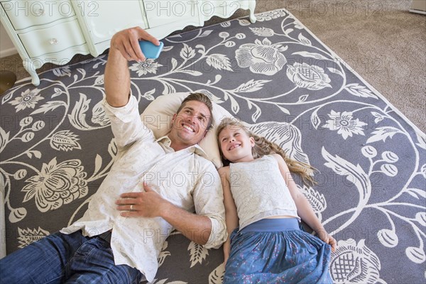 Caucasian father and daughter taking cell phone selfie on floor