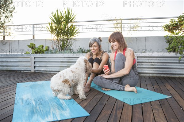 Women with dog using cell phone on exercise mat