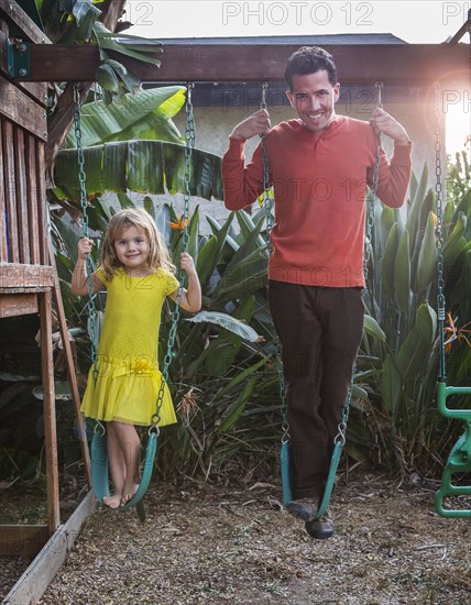 Caucasian father and daughter standing on swings