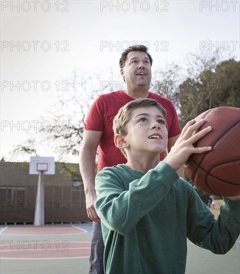 Caucasian father watching son hold basketball on court