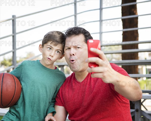 Caucasian father and son taking cell phone photograph on bleachers